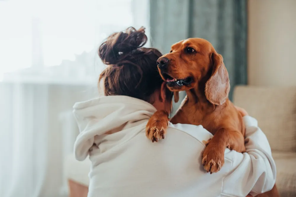 Tutora de costas abraçada ao seu cachorro, que apoia as patas no ombro dela